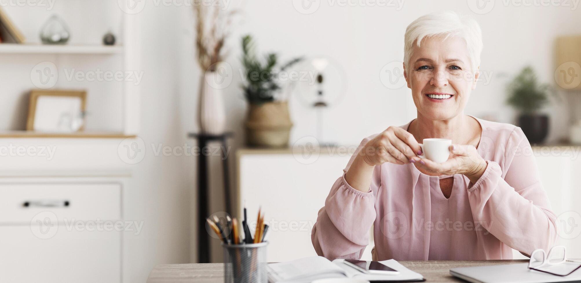 Peaceful aged business lady having coffee break while working from home, copy space photo
