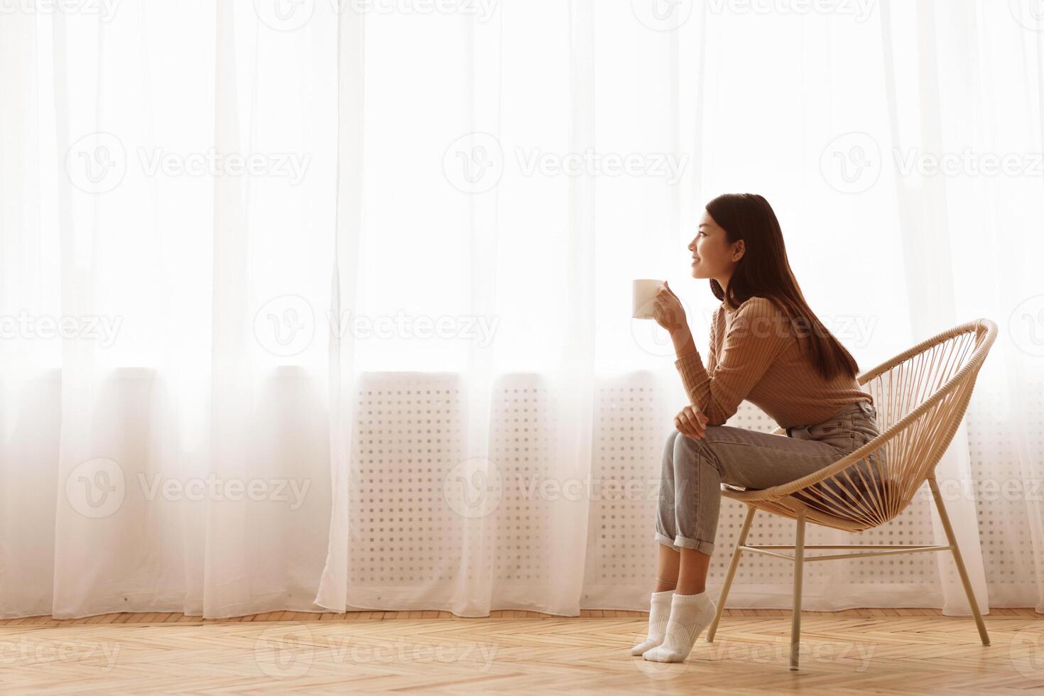 Young Girl Sitting In Modern Chair, Enjoying Coffee In Front Of Window, Side View photo