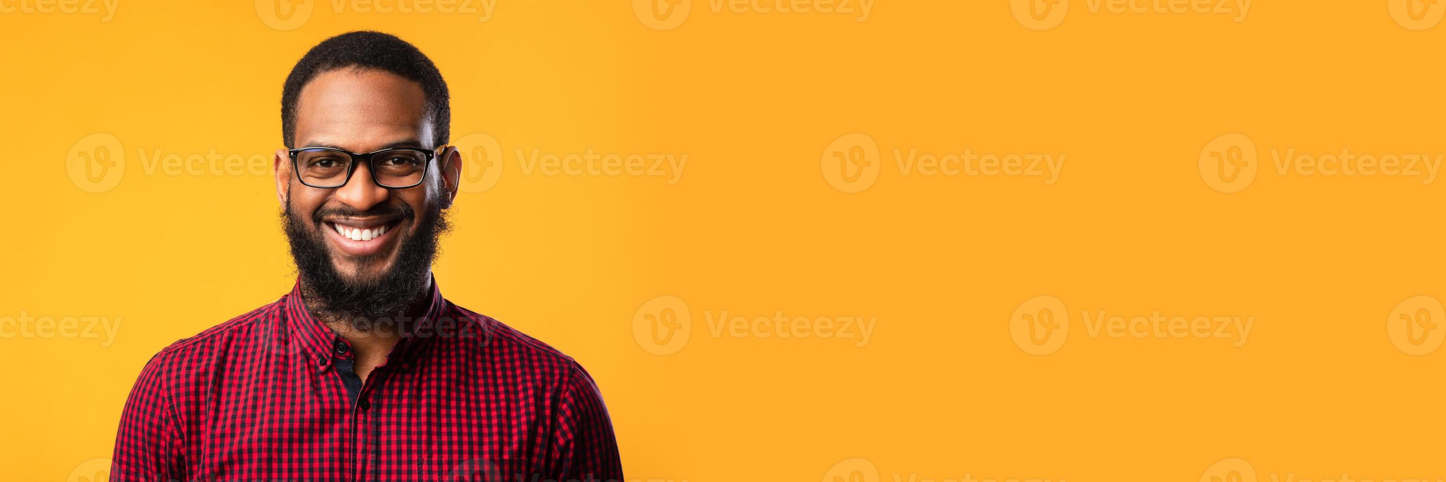 Closeup headshot of content black guy in eyewear looking at camera with smile over yellow studio wall, copy space photo