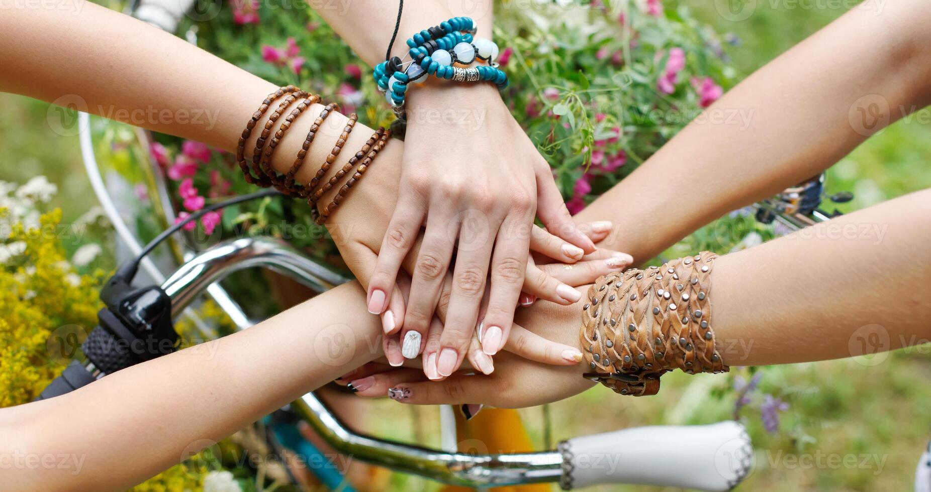 Girl Friendship. United hands of young females. Stylish girlfriends in boho hippie bracelets near bicycle handlebar, top view. Togetherness and support, youth fashion and active lesiure. photo