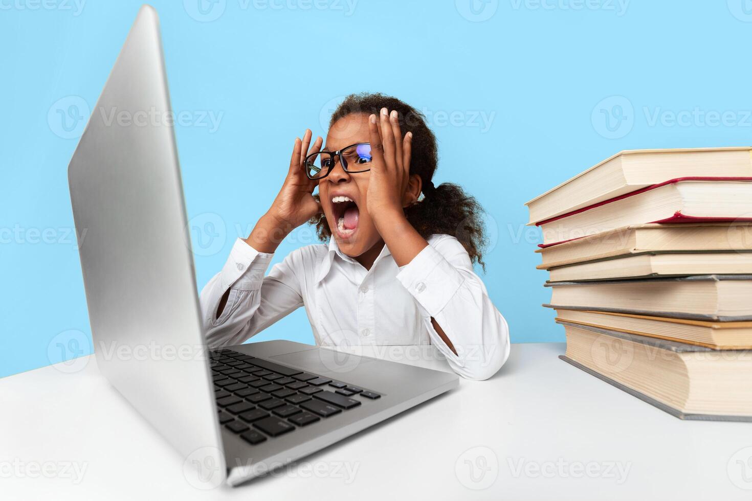 Angry African American Schoolgirl Screaming At Laptop Doing Homework Over Yellow Background In Studio. School Overwork And Stress photo