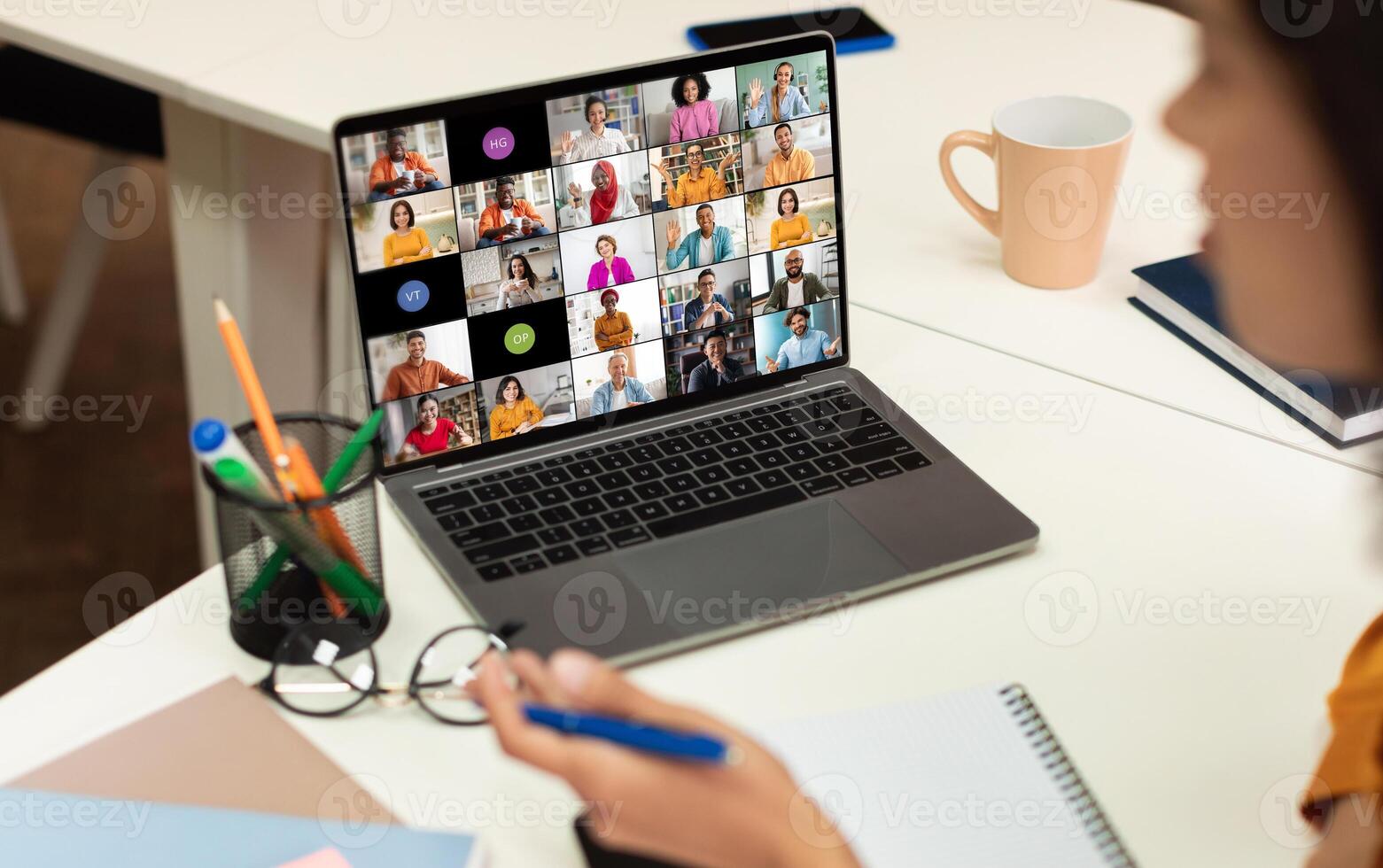 A laptop screen displays a conference call with multiple participants of various backgrounds and ethnicities, all appearing in separate squares. photo
