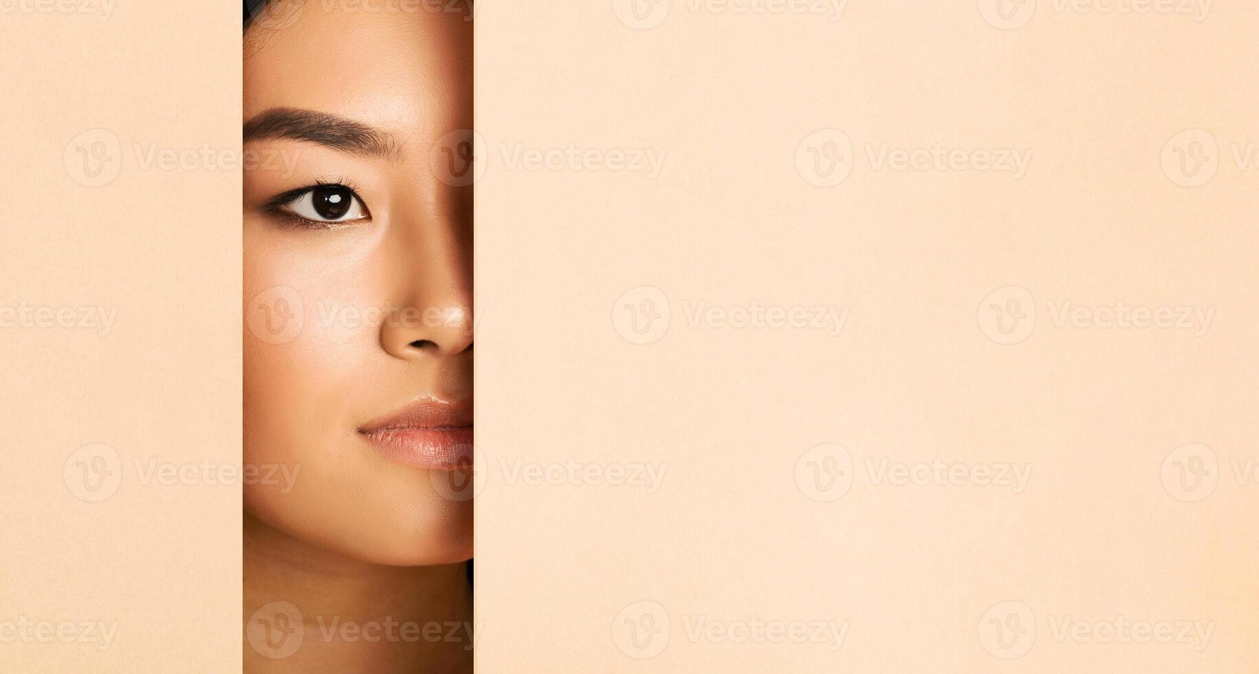 Asian woman face peeking from behind a piece of beige paper. Only her eye and part of her face are visible, creating a sense of mystery and intrigue, copy space photo