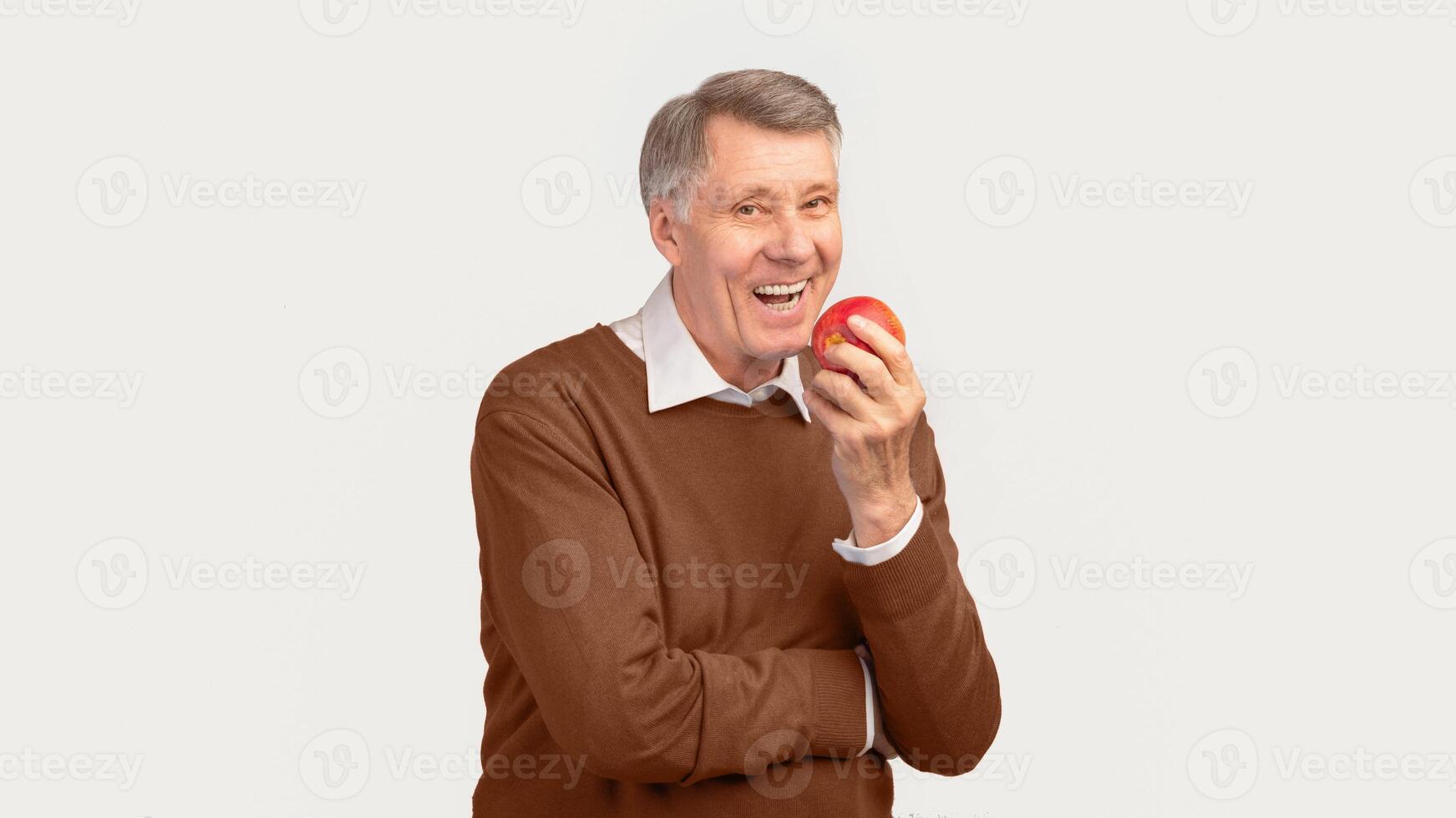 Smiling Senior Man Biting Apple Standing Over White Studio Background. Healthy Teeth In Old Age. Panorama, Free Space photo