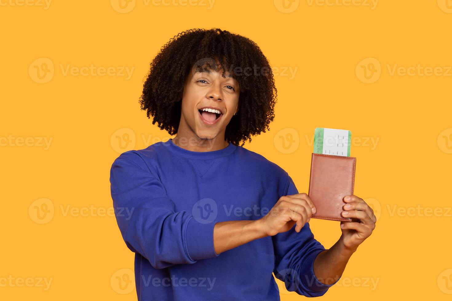 A cheerful young man is shown excitedly holding up a passport and a boarding pass. He is wearing a blue sweatshirt. The background is a solid yellow color photo