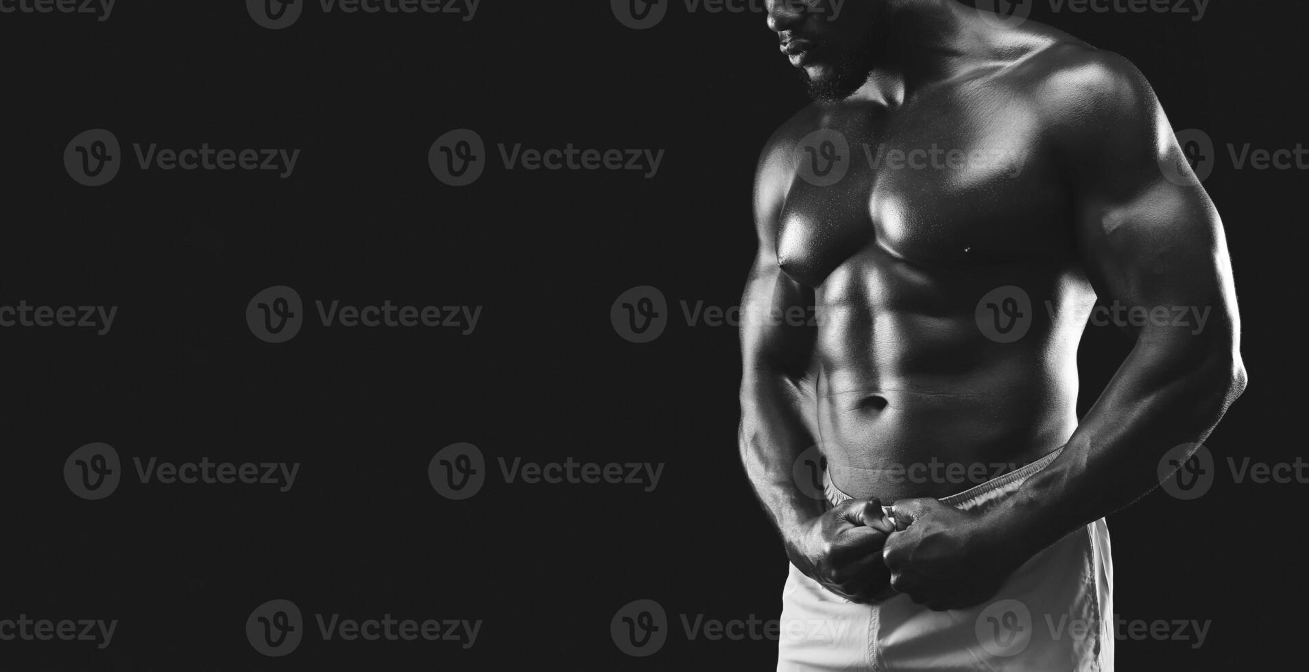 A black and white image of a muscular man posing in a dark studio setting, showcasing his defined physique. photo