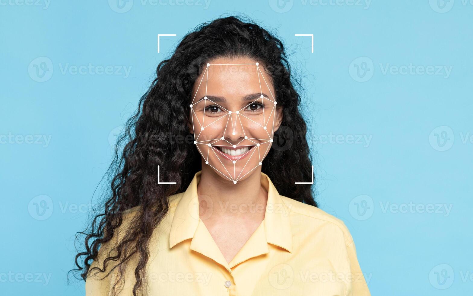 A middle eastern woman with curly hair smiles while a facial recognition overlay appears on her face against a blue background. photo