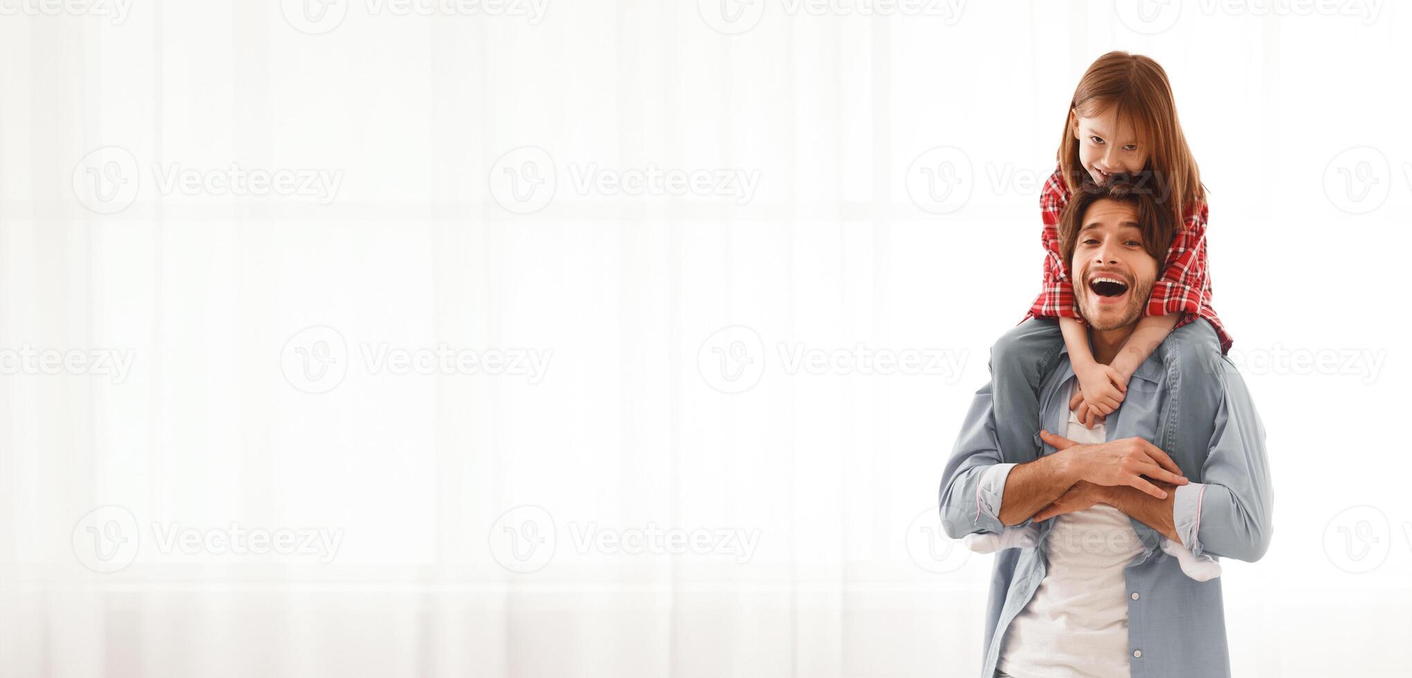 Adorable little girl sitting on emotional daddy shoulders and hugging him over big window at home photo