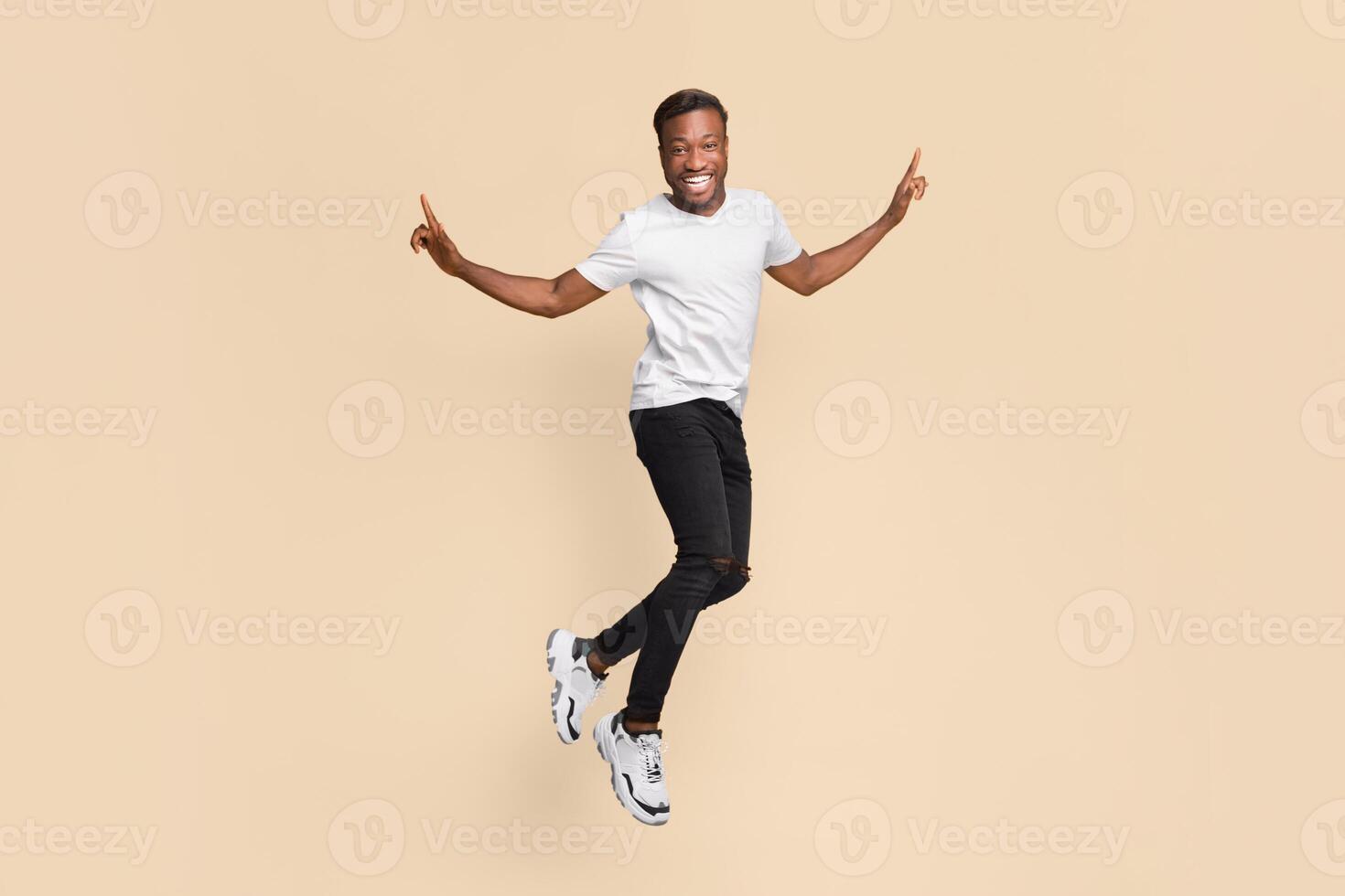 Joyful Young Afro Man Having Fun Jumping In Air Over Yellow Studio Background. photo
