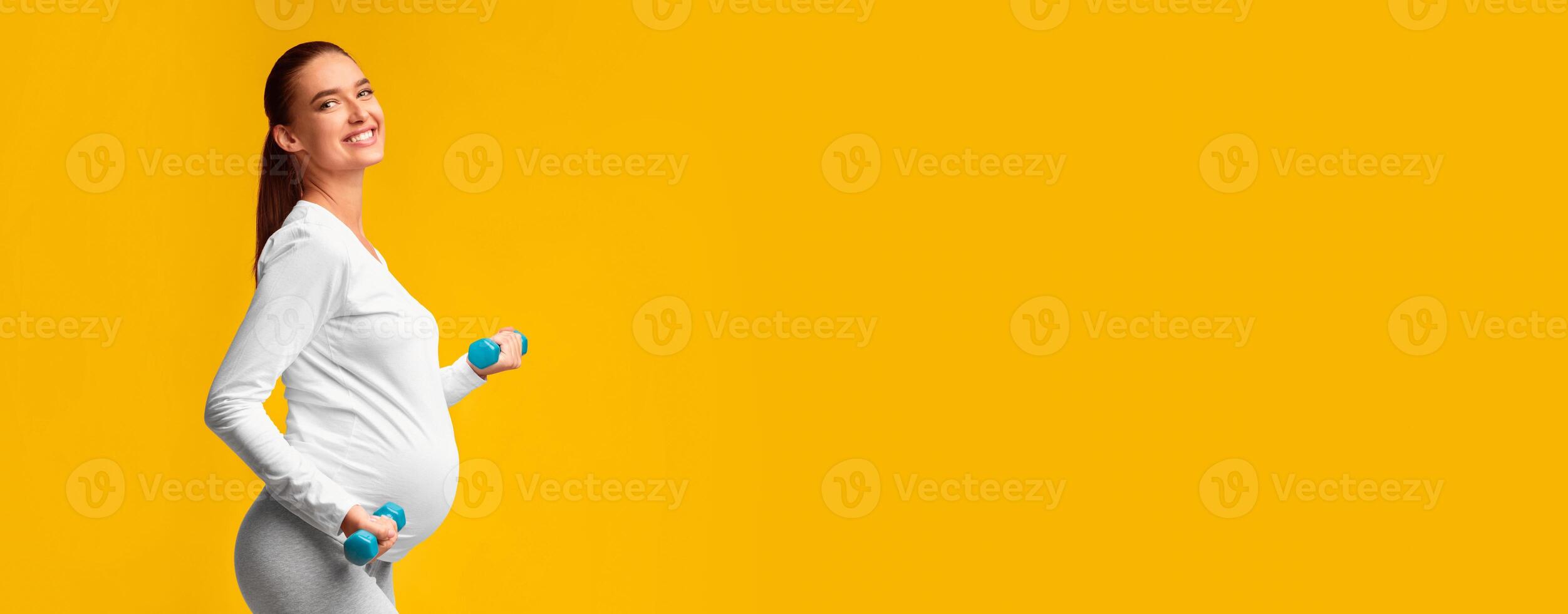 Pregnancy Fitness. Pregnant Girl Exercising With Dumbbells Smiling Standing Over Pink Studio Background. Side View, Panorama, Copy Space photo