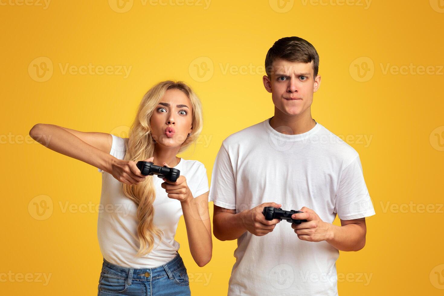 Young guy and girl emotionally playing game with joysticks, grimacing in excitement over yellow background. Panorama photo