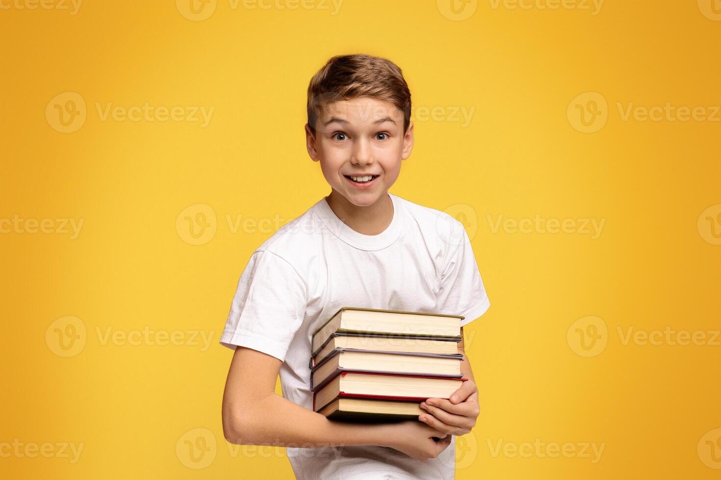 Enjoying remote education. Teen boy smiling with heap of books in hands, orange studio background photo