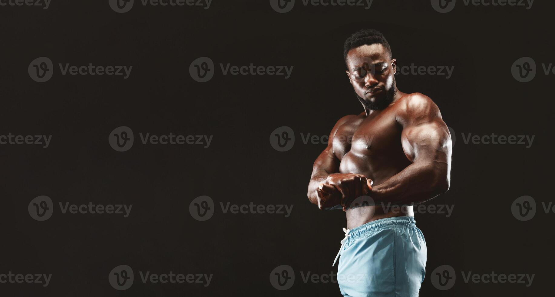 African bodybuilder flexing his muscles, showing biceps in studio, black background photo