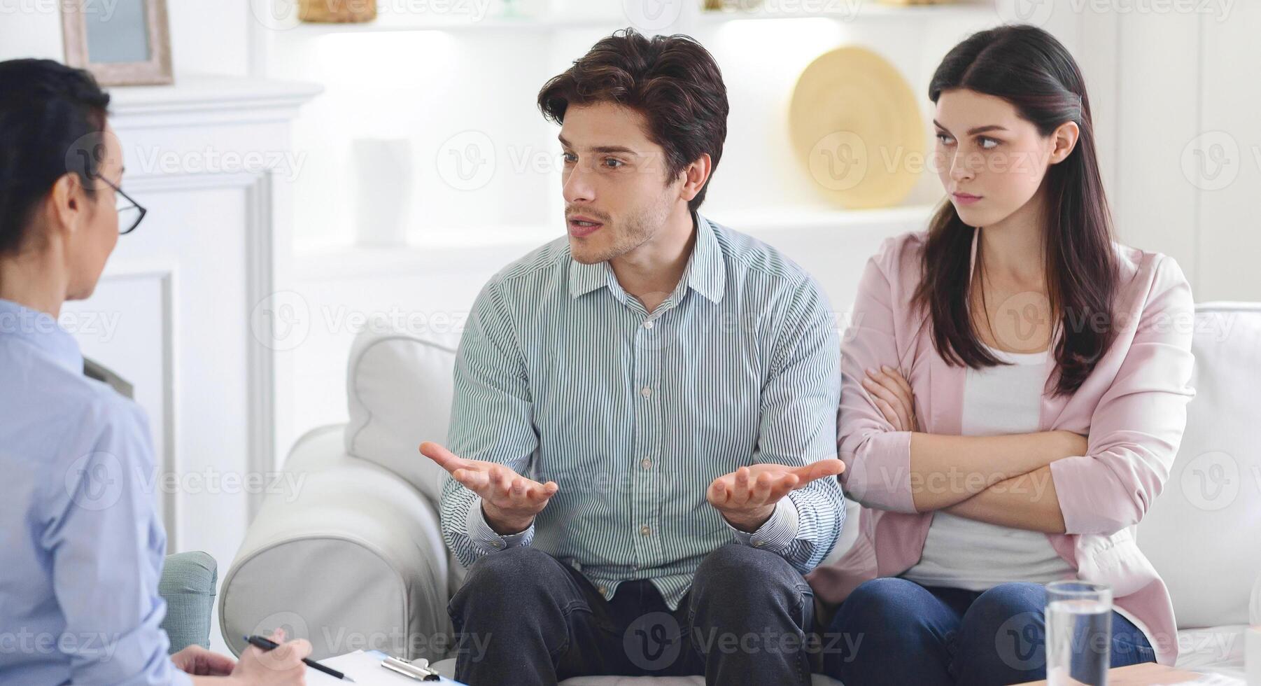 A man and woman are engaged in a counseling session on a couch, conversing with a counselor. They appear focused and attentive as they discuss issues in a calm and professional setting. photo