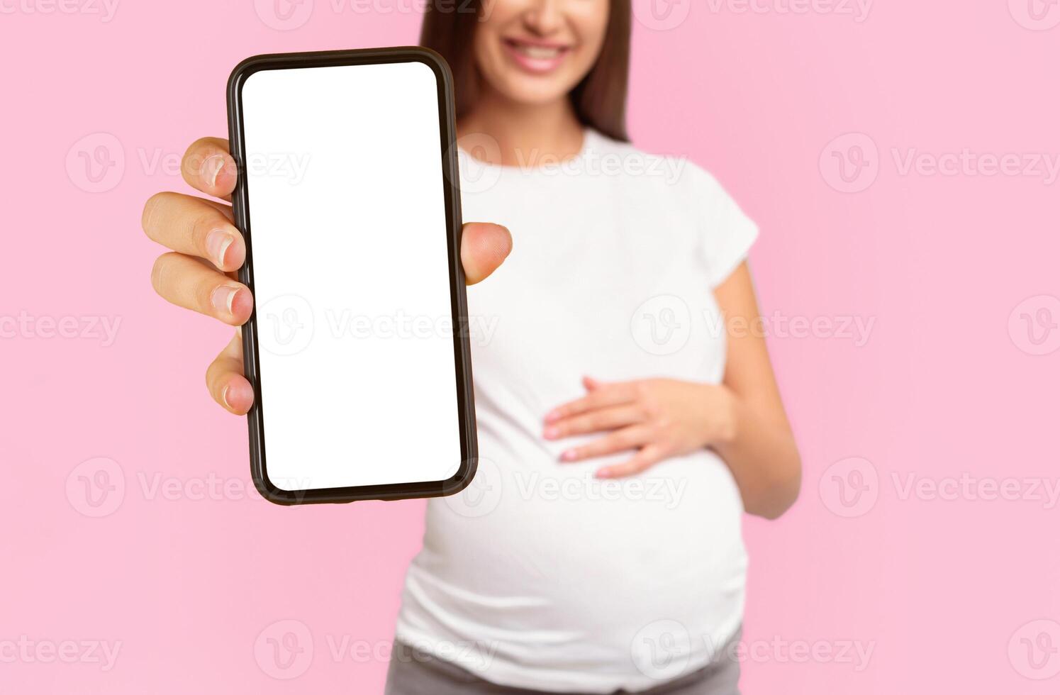 Unrecognizable Pregnant Girl Offering Green Apple To Camera Standing Touching Belly Over White Studio Background. Cropped photo