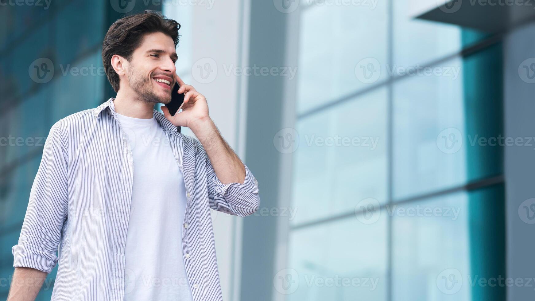 Always In Touch. Happy Young Man Talking On Cellphone While Walking Near Airport Terminal photo