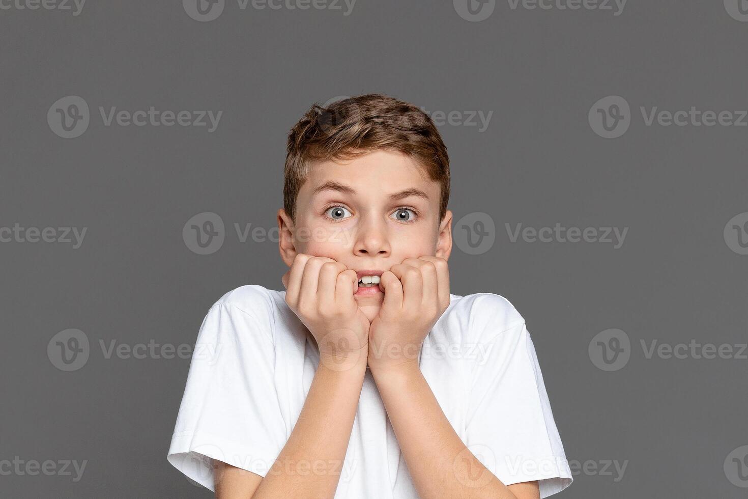 A teenage boy expressing surprise, hands on cheeks, isolated on a grey background. This image captures a youngster's candid reaction photo