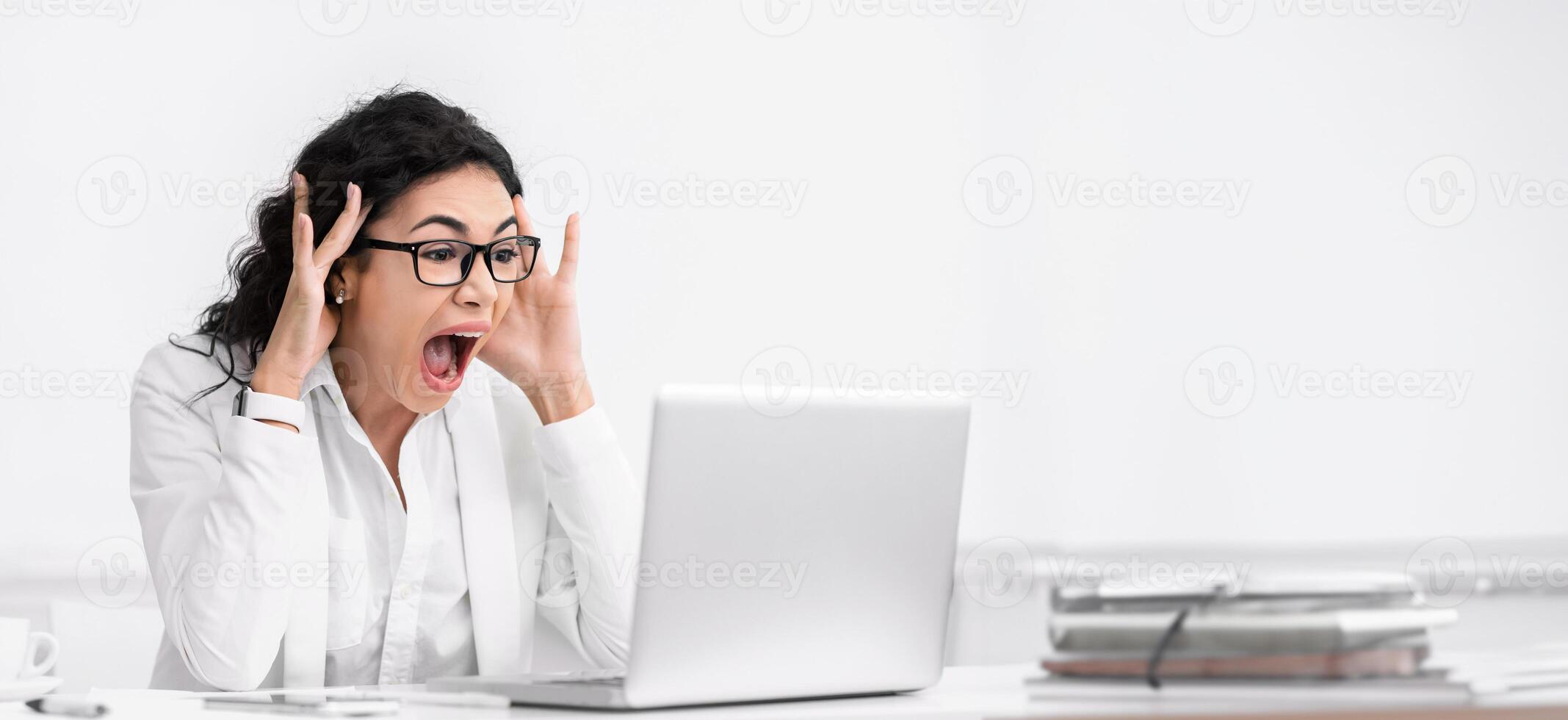 Shocking News. Amazed mexican businesswoman looking at laptop computer with open mouth and eyes. Copy space photo