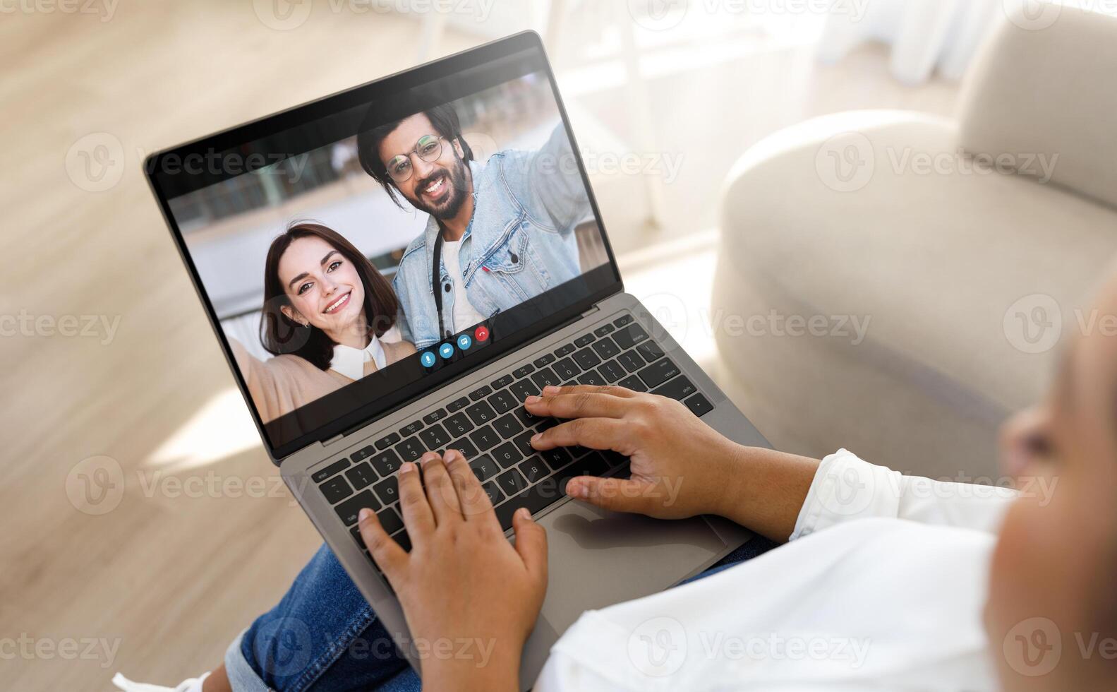Black woman sits on a couch in her home and chats with her friends on a laptop. She is smiling and appears to be enjoying the conversation photo