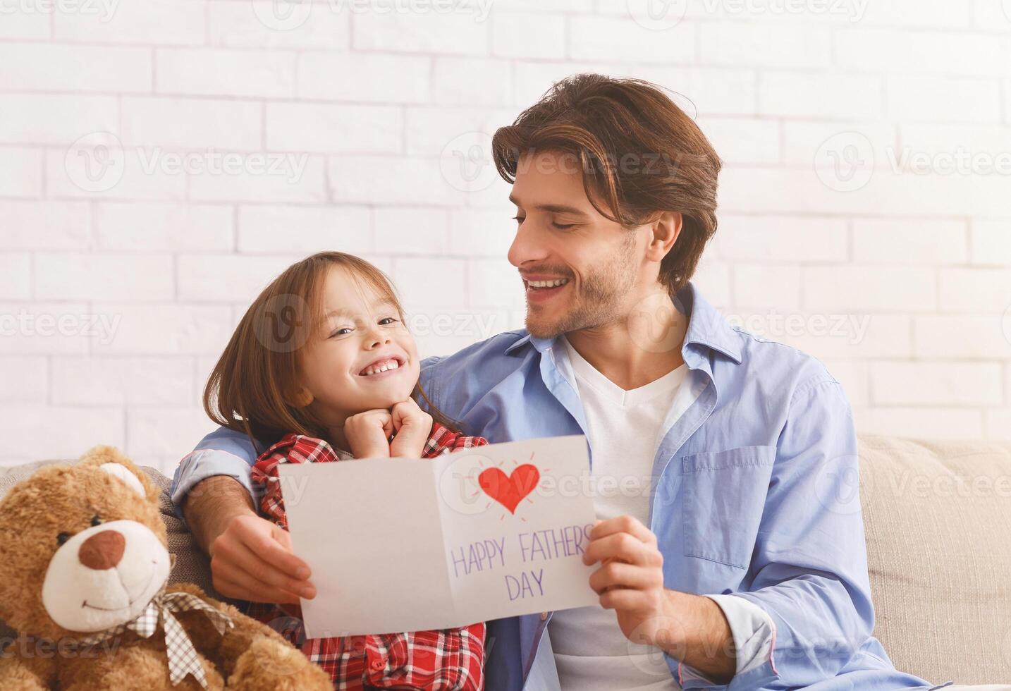 Happy man and little girl sitting on sofa at home, celebrating Father's Day, dad holding gift card and present, free space photo