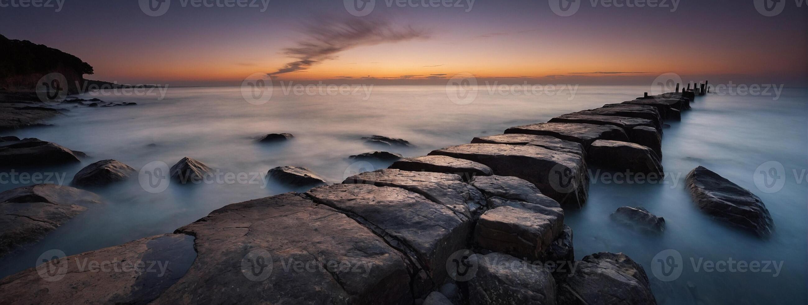 A long exposure photograph of rocks in the ocean at sunset photo
