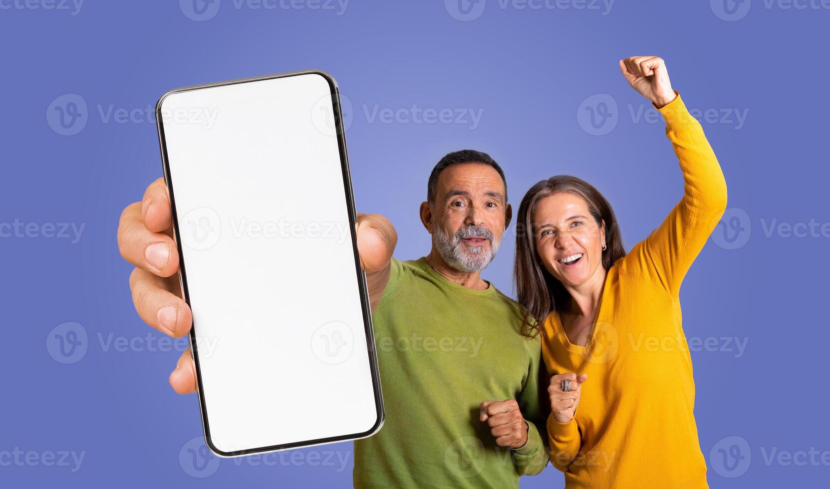 This image features mature couple posing excitedly while holding a smartphone with a blank screen in front of a purple background photo