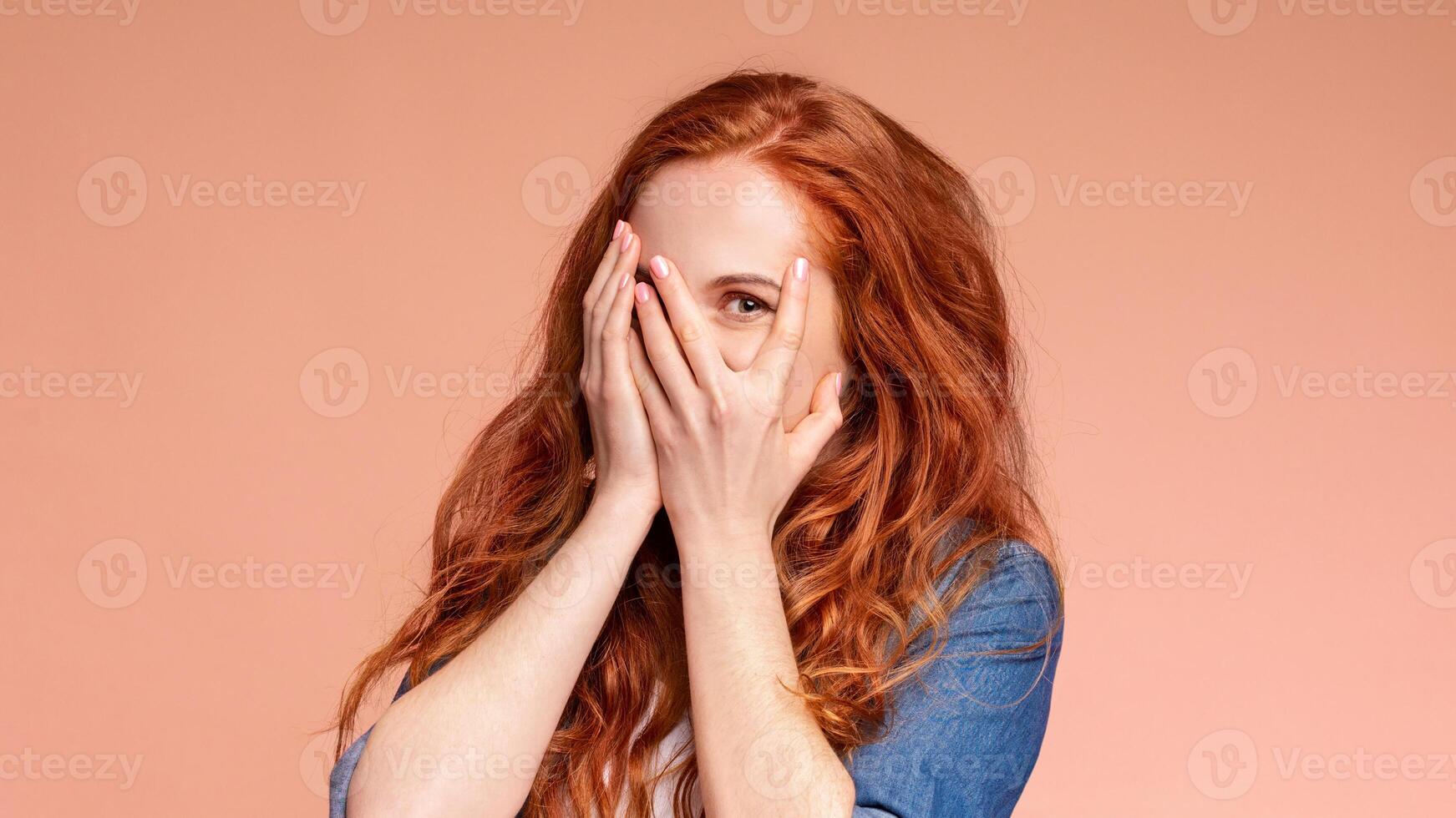A woman is sitting with her hands covering her face, blocking her eyes. She appears to be playful, isolated on colorful background photo