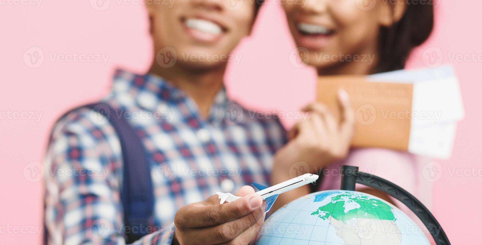 Teenage couple planning and preparing for journey with globe on pink background photo