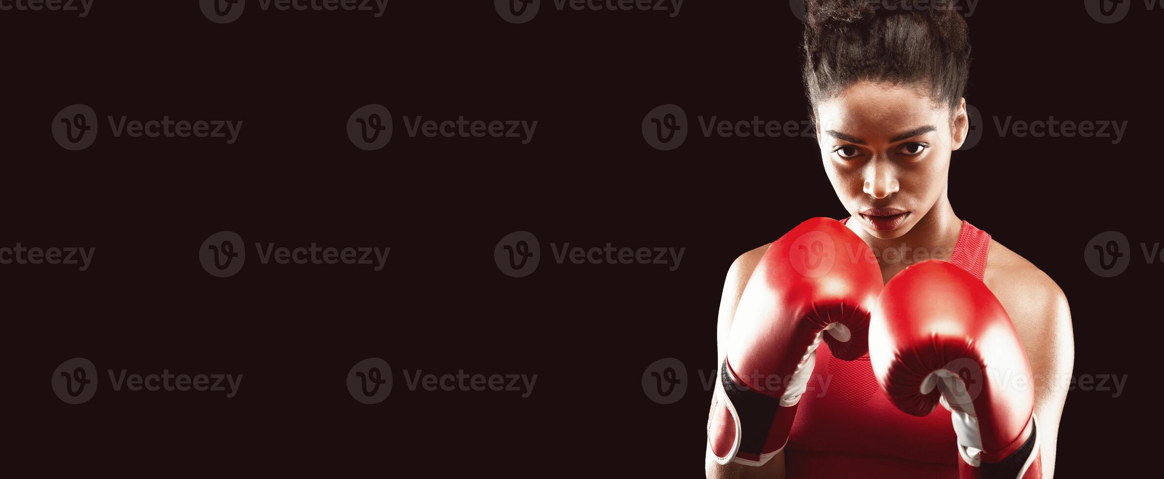 Close up of young african woman in boxing gloves over black background photo