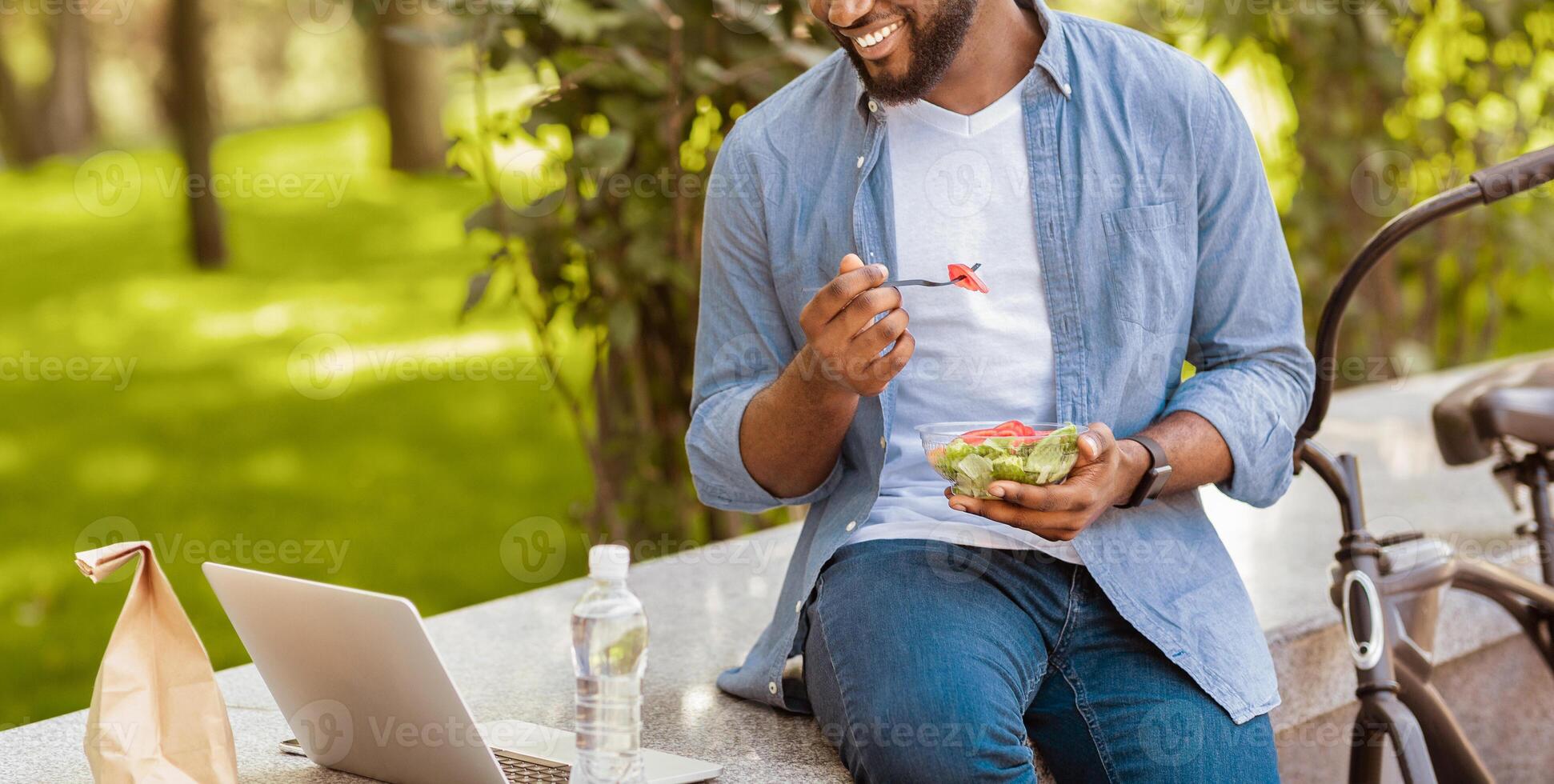 Outdoor Leisure. Unrecognizable Afro Man Eating Lunch And Watching Movie On Laptop In Park, Enjoying Spending Time Outside, Cropped Image, Panorama photo