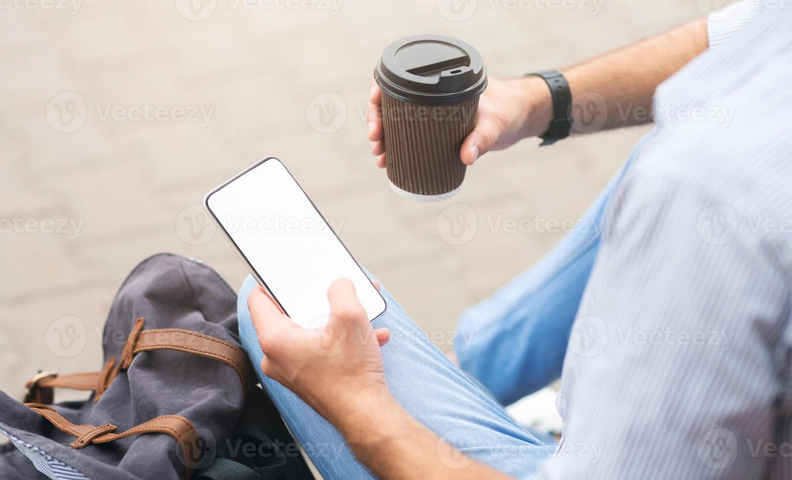 Takeout Coffee And Smartphone With Blank Screen In Hands Of Unrecognizable Man Sitting Outdoors, Over Shoulder Shot, Cropped photo