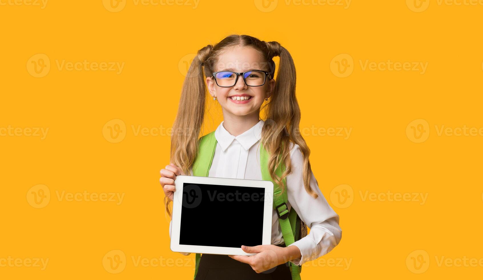 School Apps And Gadgets. Cute Elementary Student Girl Showing Blank Tablet Screen On Yellow Background. Empty Space For Text photo