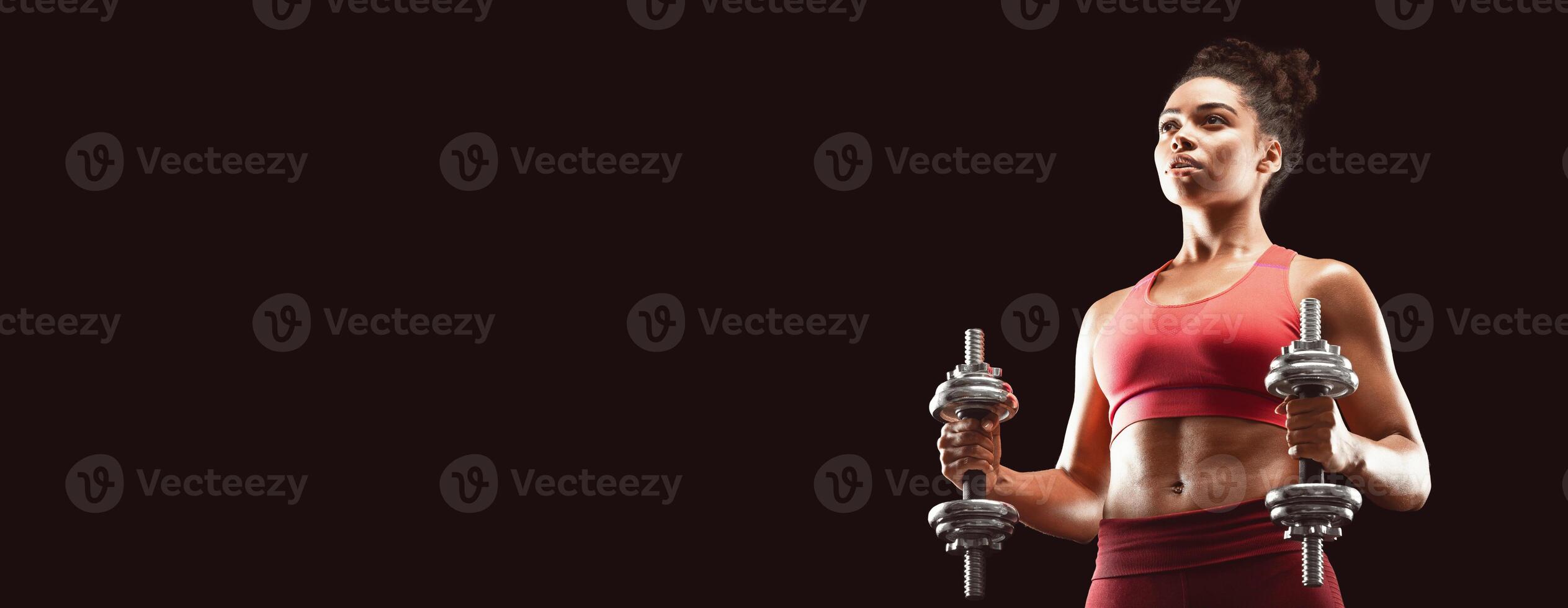 Athletic afro woman having work out with barbells over black background, empty space photo