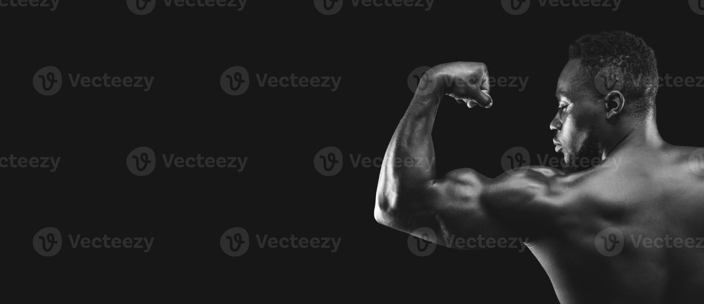 A muscular man flexes his bicep against a black background. photo