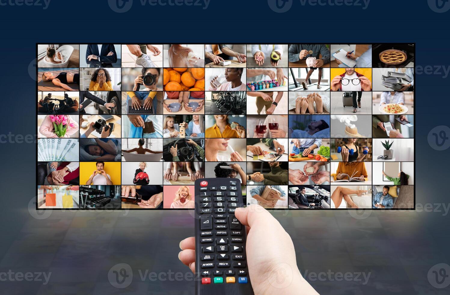 A hand holds a black remote control in front of a large screen displaying numerous images. The screen shows a grid of small videos or images depicting various scenes and activities photo