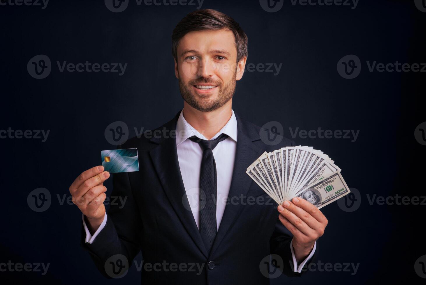 A man in a suit holds a credit card in one hand and a fan of cash in the other. photo