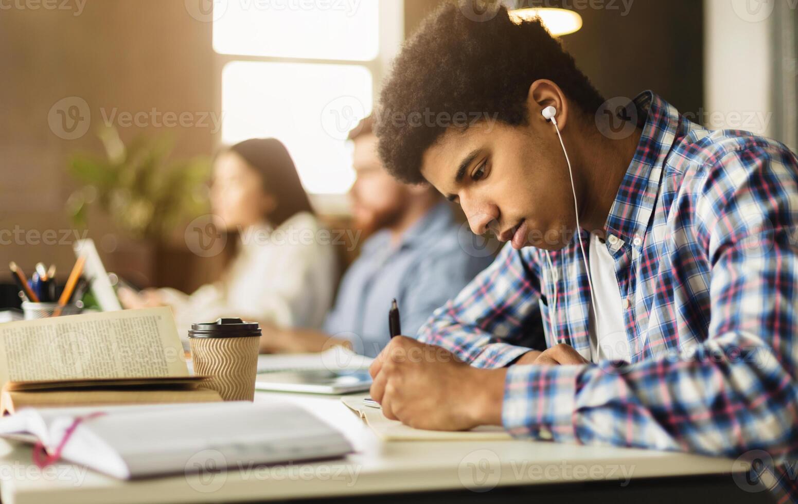Black guy taking notes, preparing for classes in college library, studying together with classmates photo