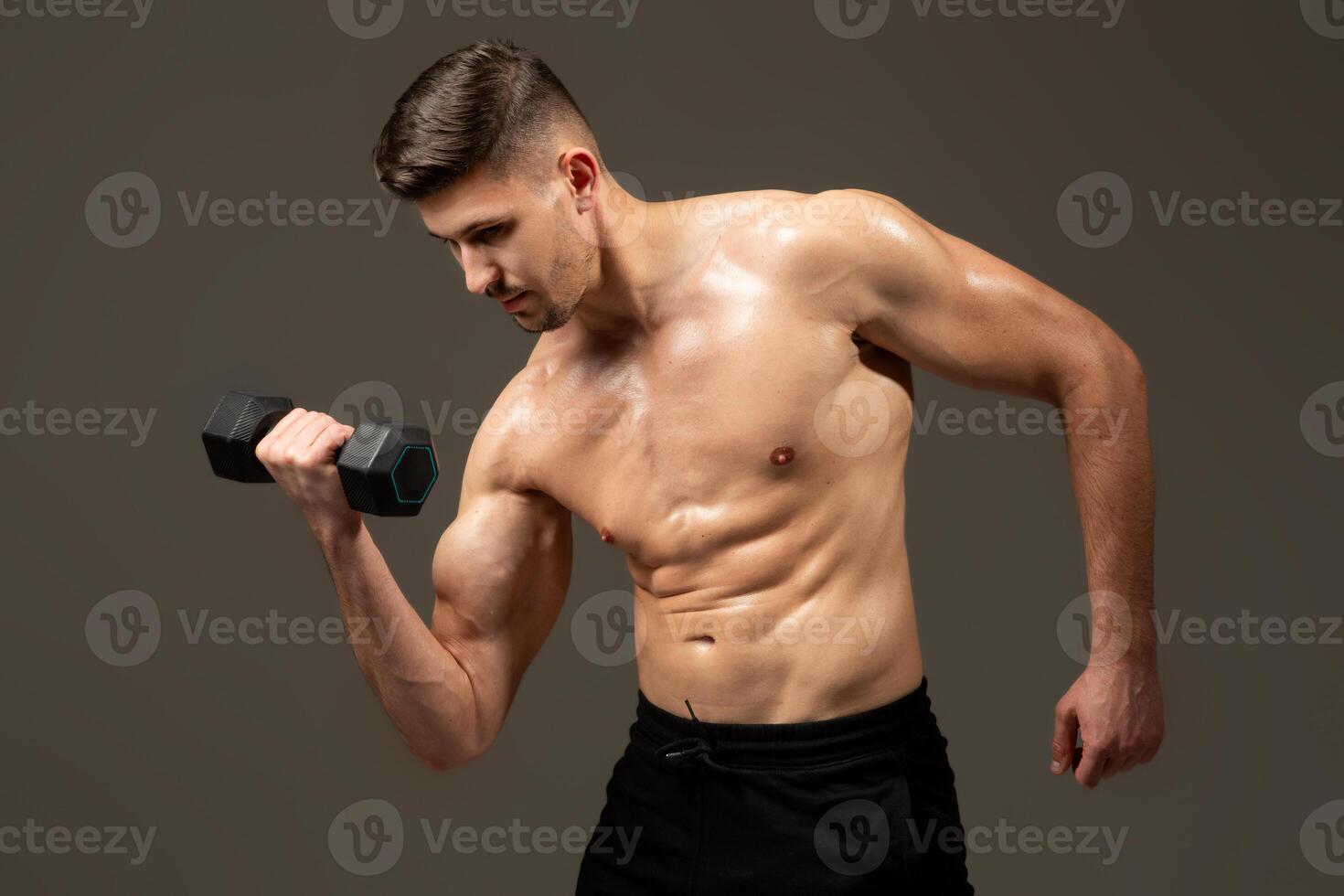A man is lifting a dumbbell in front of a plain gray background. He is focused and determined, showcasing strength and fitness. photo