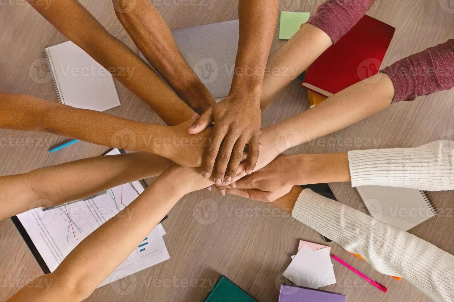 Multiracial teenagers joining hands together in cooperation, preparing common academic project, top view photo