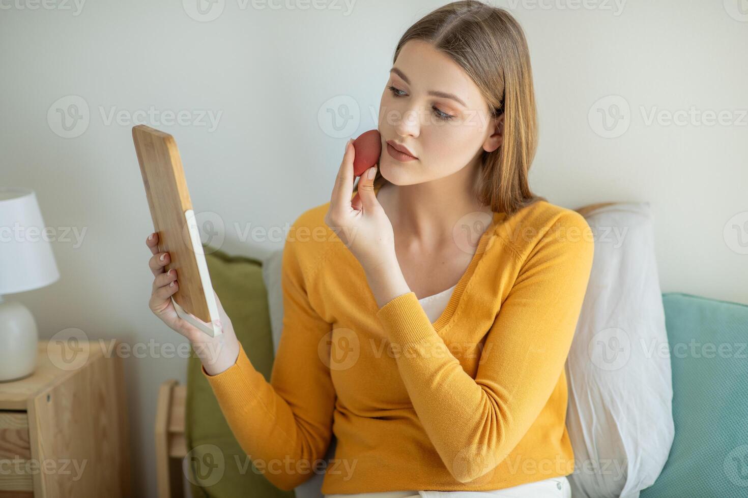 A girl is seated on a bed, gazing at her reflection in a mirror placed in front of her. She appears contemplative as she studies her own features in the reflective surface. photo