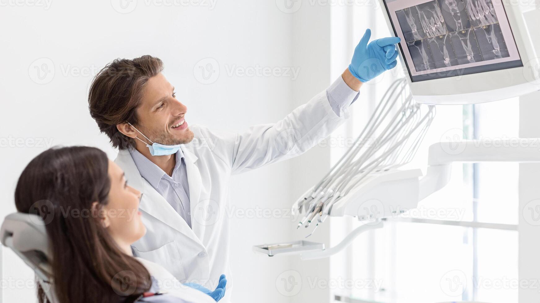 Cheerful male dentist doctor showing his patient x-ray results on lcd display, side view, copy space photo