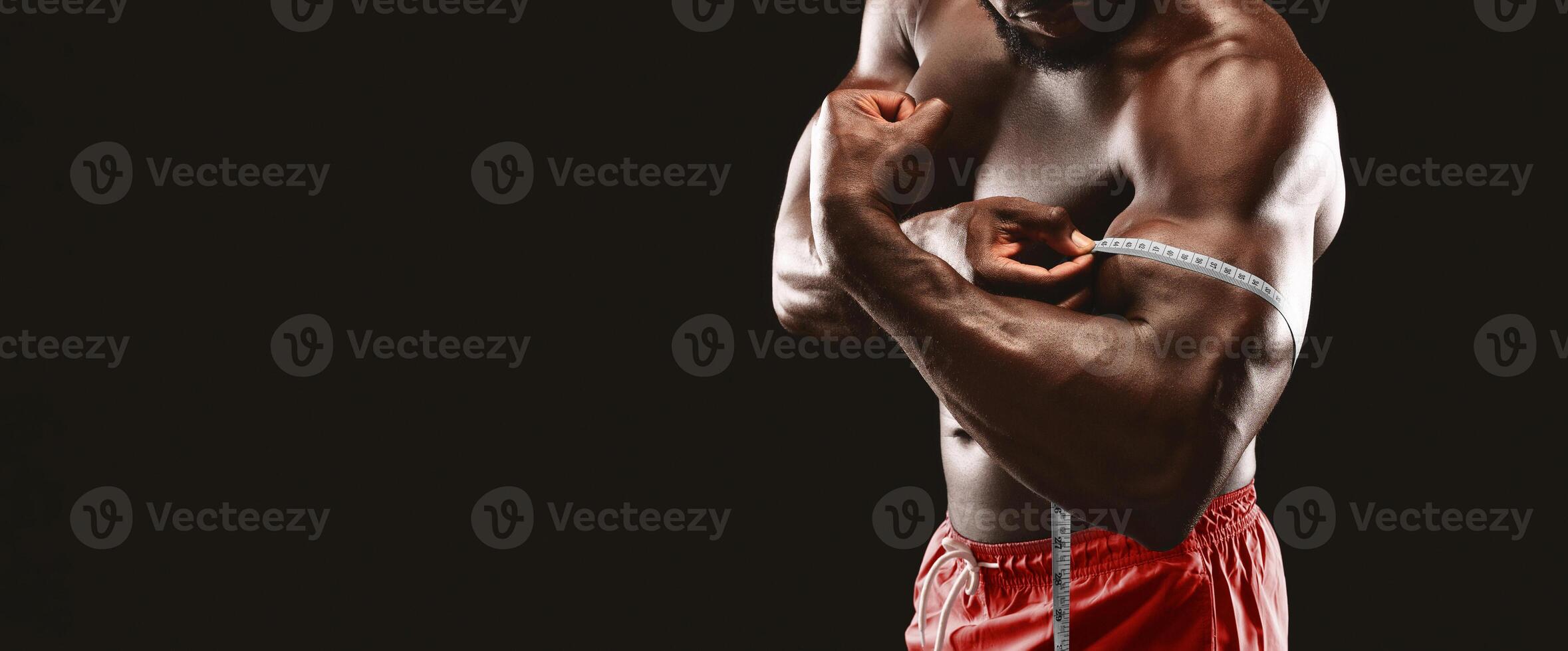 A muscular man flexes his bicep and measures it with a tape measure. photo