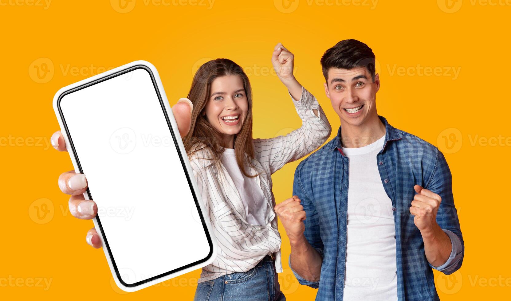 Two young people, a man and a woman, are standing in front of a solid yellow background. The woman is holding a smartphone with a blank screen. The man is standing beside her photo