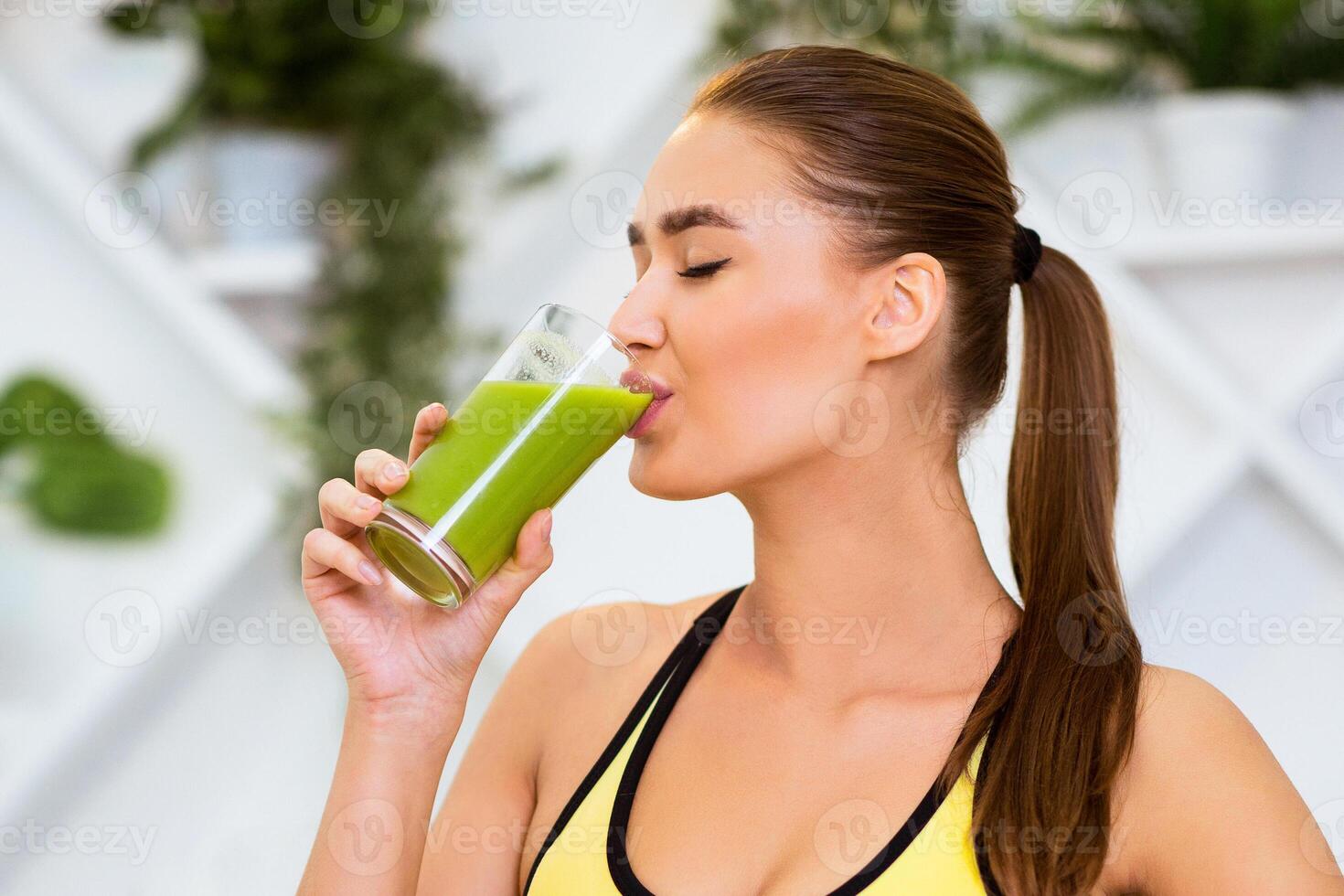 A woman drinks a refreshing green smoothie, enjoying a healthy and refreshing beverage in a bright, modern gym setting. photo