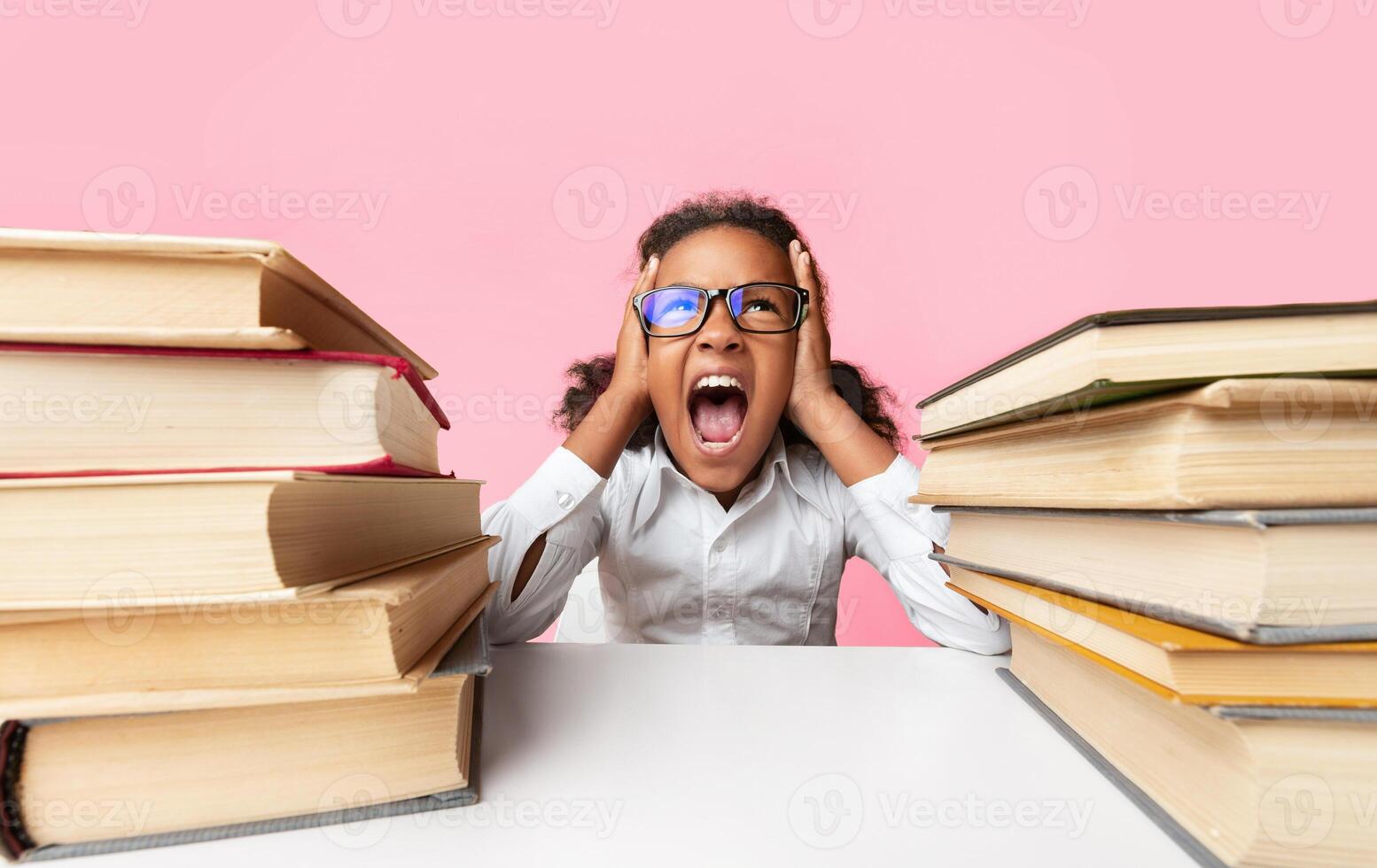 School Overload. African American Schoolgirl Shouting Clutching Head Sitting Between Two Book Stacks Over Yellow Studio Background. photo