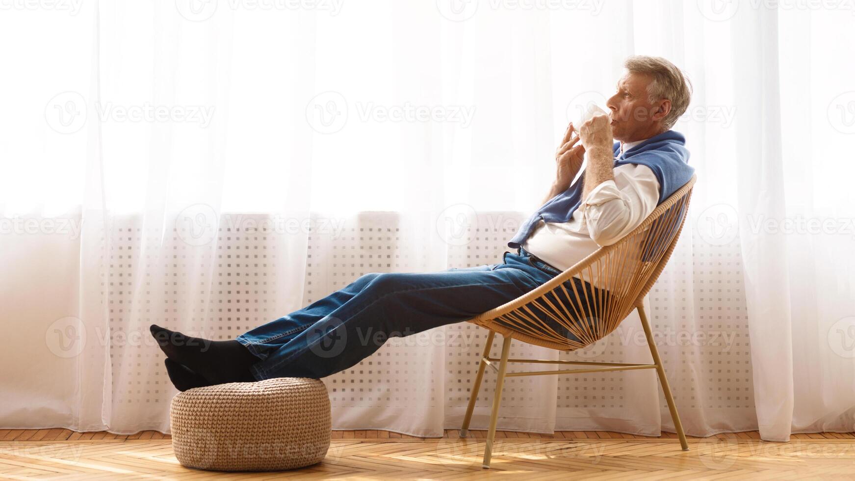 Relaxed senior man enjoying morning coffee on chair near window, side view, copy space photo