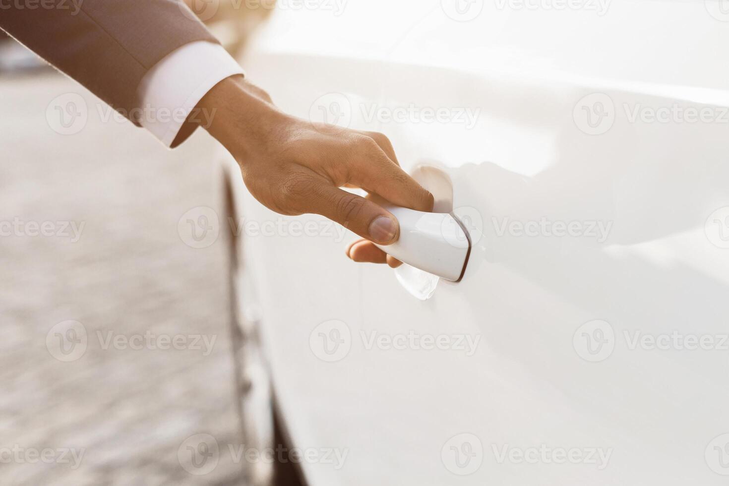 A close-up image of a persons hand opening the door of a white car. The sunlight is shining brightly on the car and the persons hand. photo