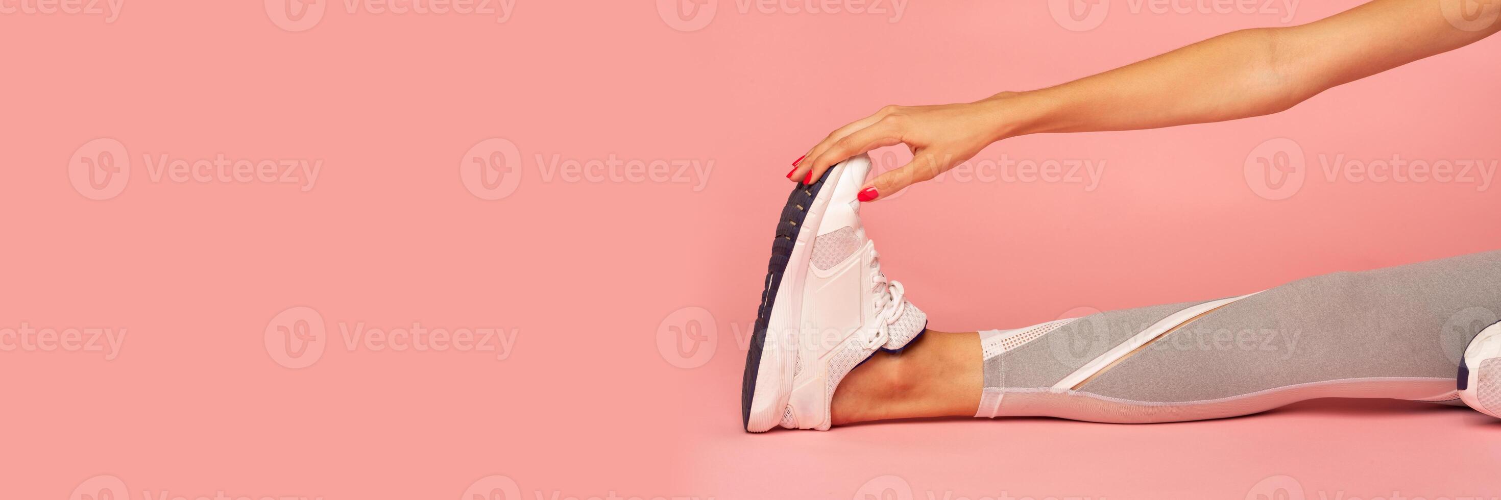 Unrecognizable Lady Stretching Leg Sitting On Floor During Fitness Workout Over Pink Studio Background. Cropped, Panorama With Copy Space photo