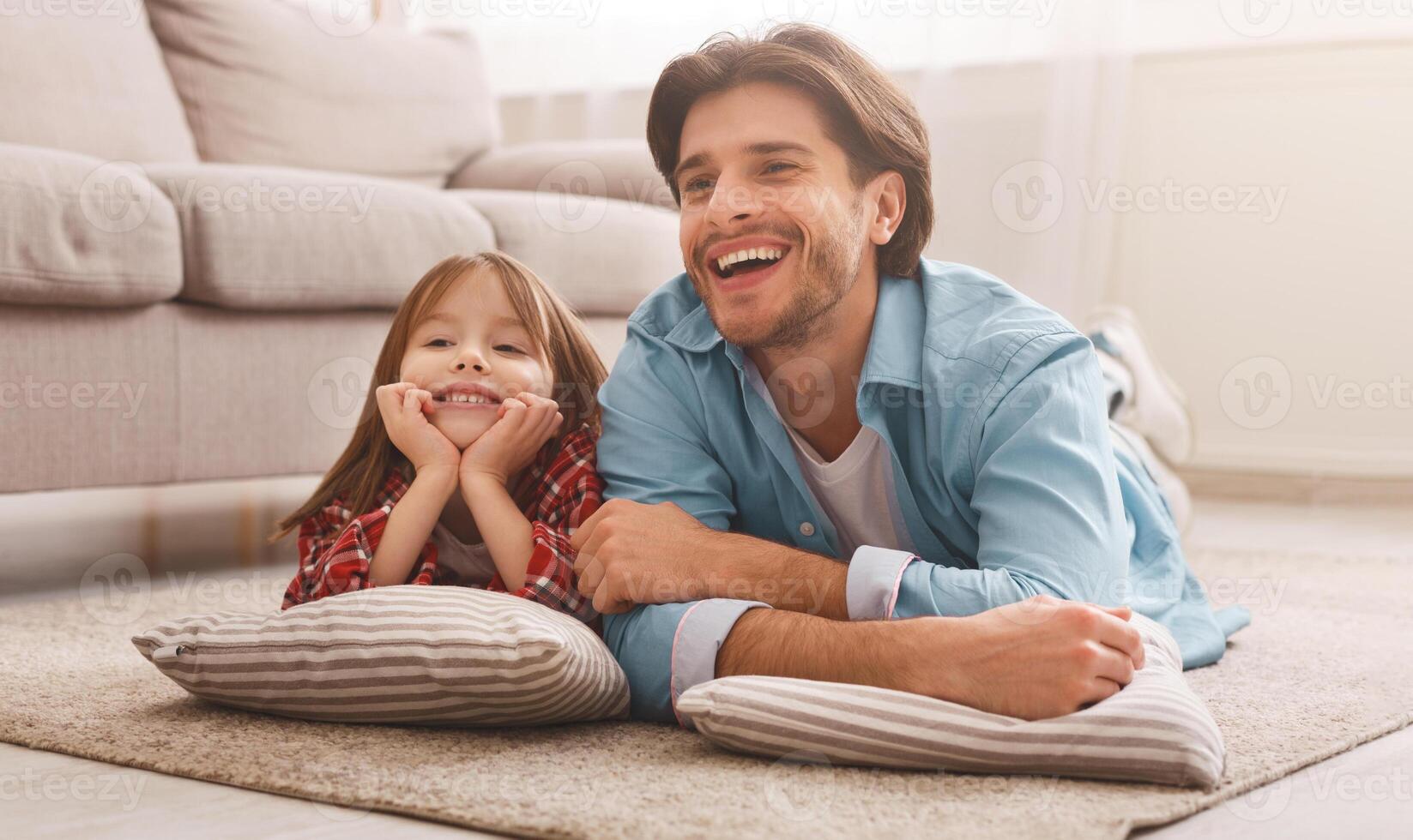 Happy family father and little daughter watching cartoons, lying on floor at home, free space photo
