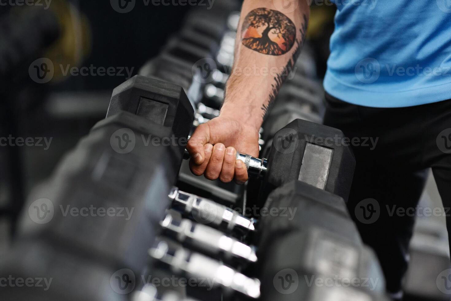 Closeup shot of muscular male arm picking up heavy dumbbell from equipment rack in modern gym, panorama photo